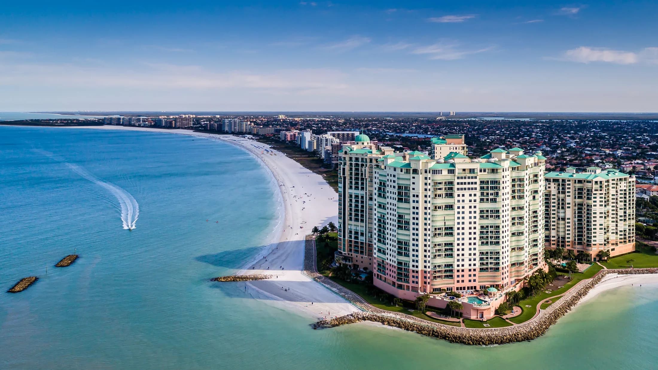 Aerial view of Marco Island beachfront towers and curved white-sand shoreline.